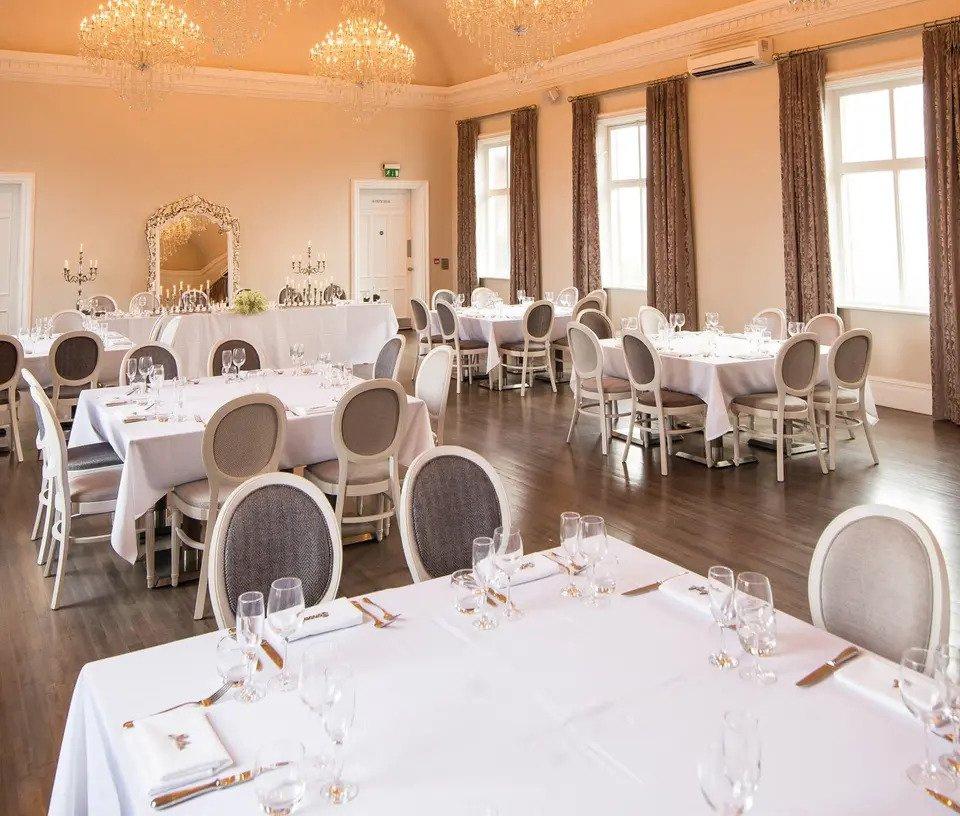 Ballroom with white tables, grey chairs and chandeliers