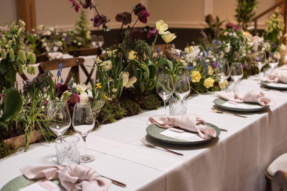 Glasses, cutlery, plates and napkins are set on a table with a beautiful floral centrepiece