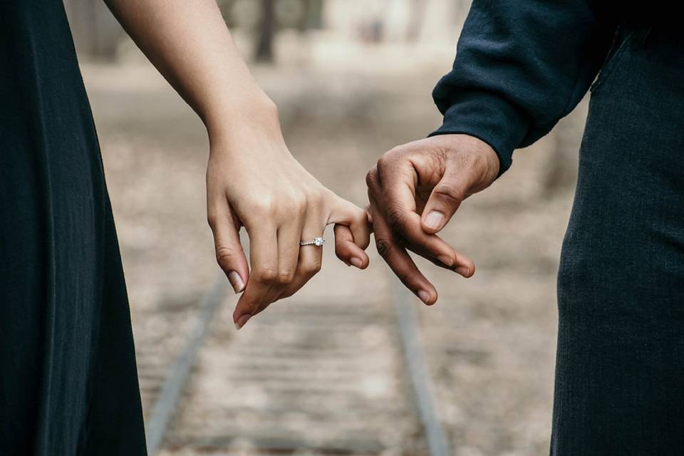 Couple standing on train tracks with hands linking whilst showing off woman's engagement ring