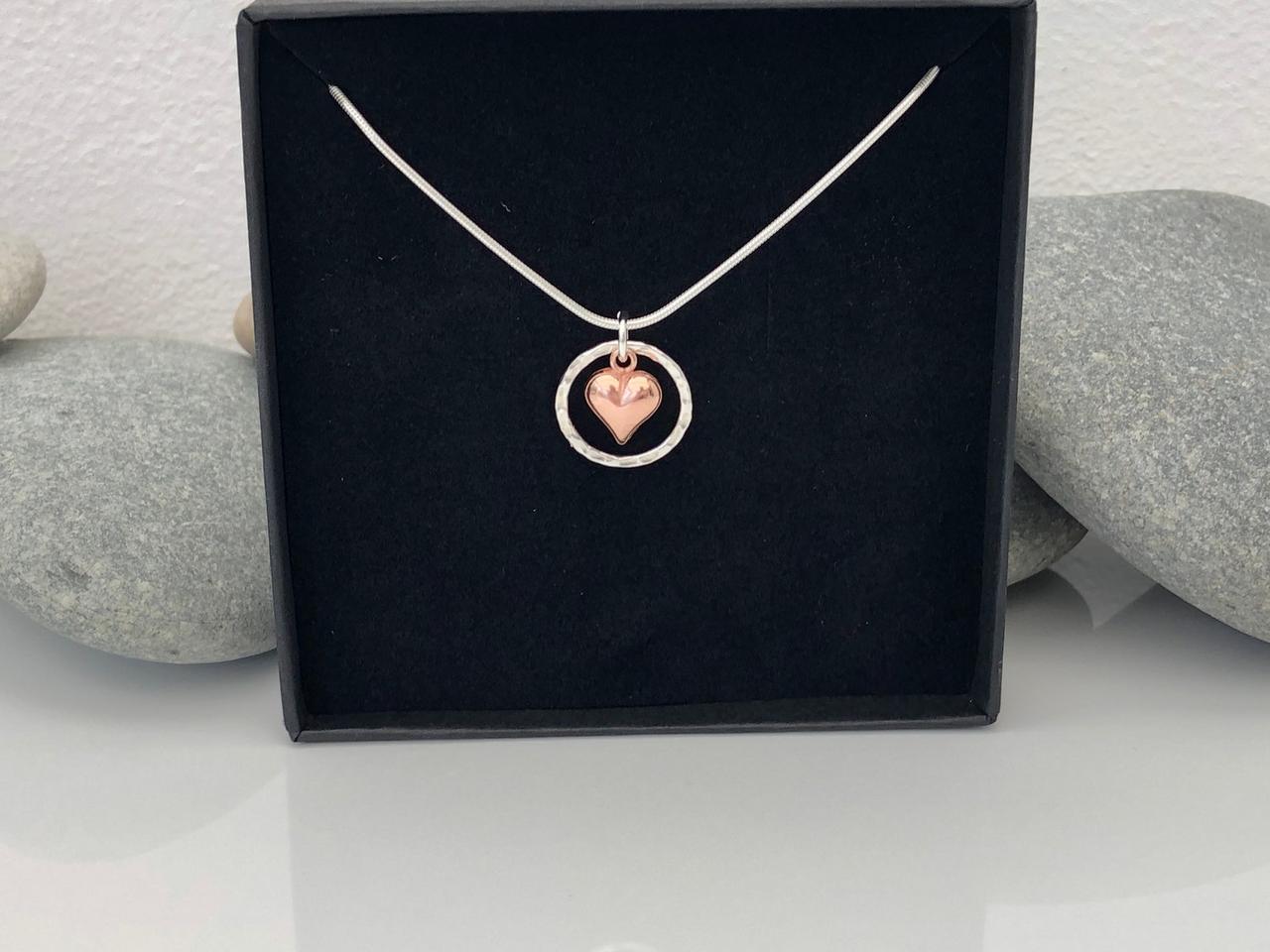 A sterling silver circle pendant with a rose gold heart hanging in the centre