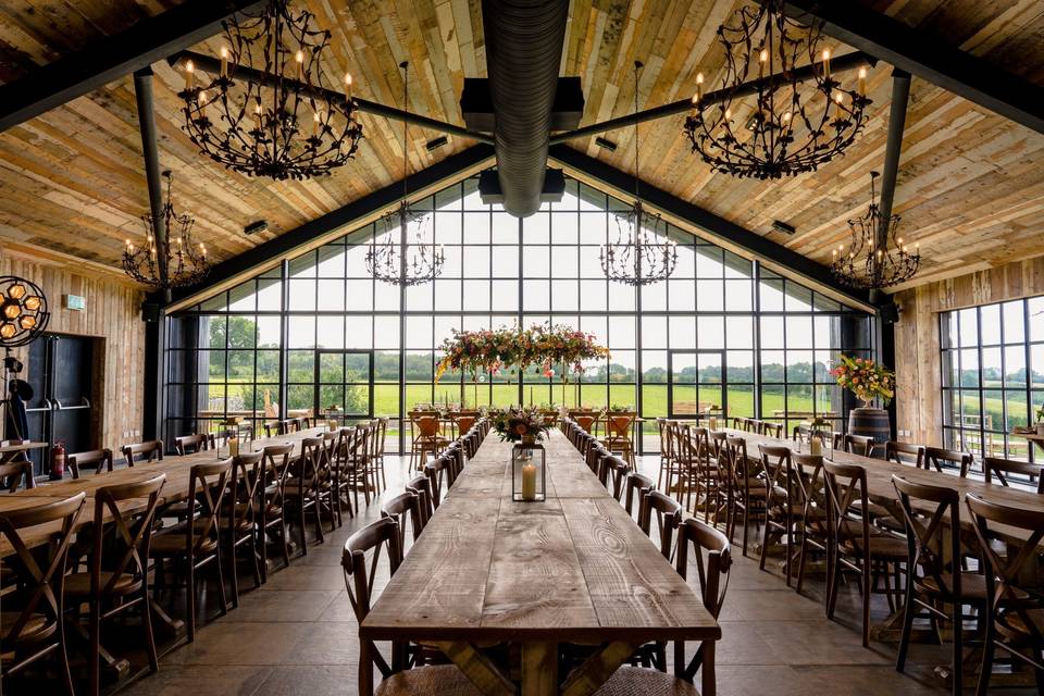 A large modern barn with floor-to-ceiling windows, metal chandeliers, and picturesque views.