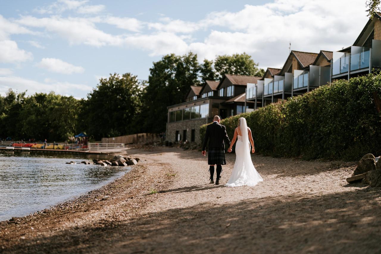 A newlywed couple walking along the beach at The Lodge in Loch Lomond.