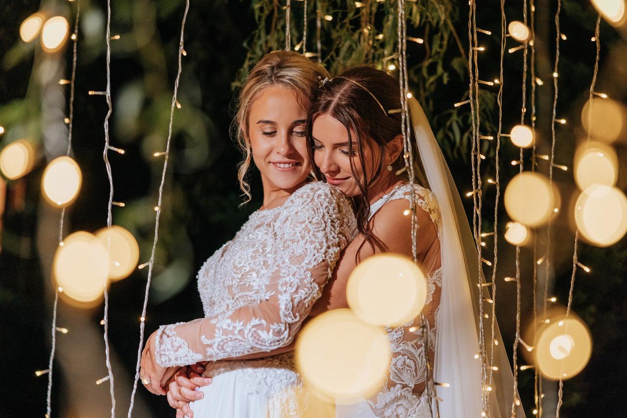 two brides embracing under fairy lights on their wedding day