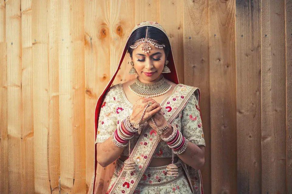 bride dressed in traditional Indian wedding attire with her eyes closed in front of a wooden background