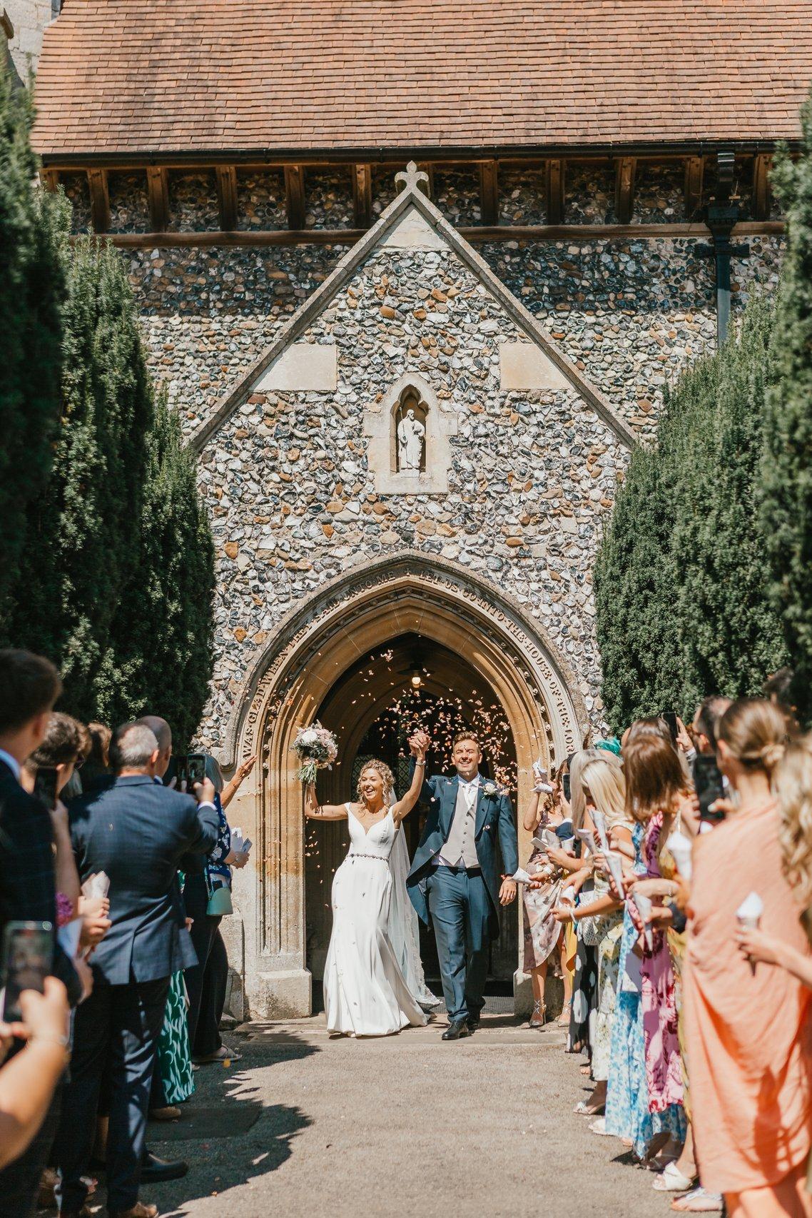The bride and groom leave the church as their guests throw confetti