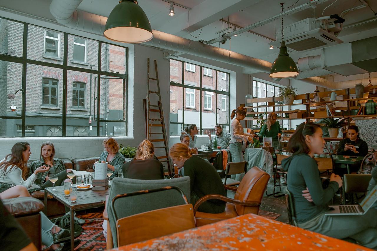 The insideof a cafe with wooden furniture, house plants and people sitting and drinking coffee