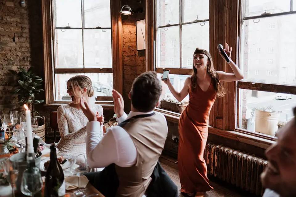 A bridesmaid delivering a funny wedding toast with everyone around her clapping