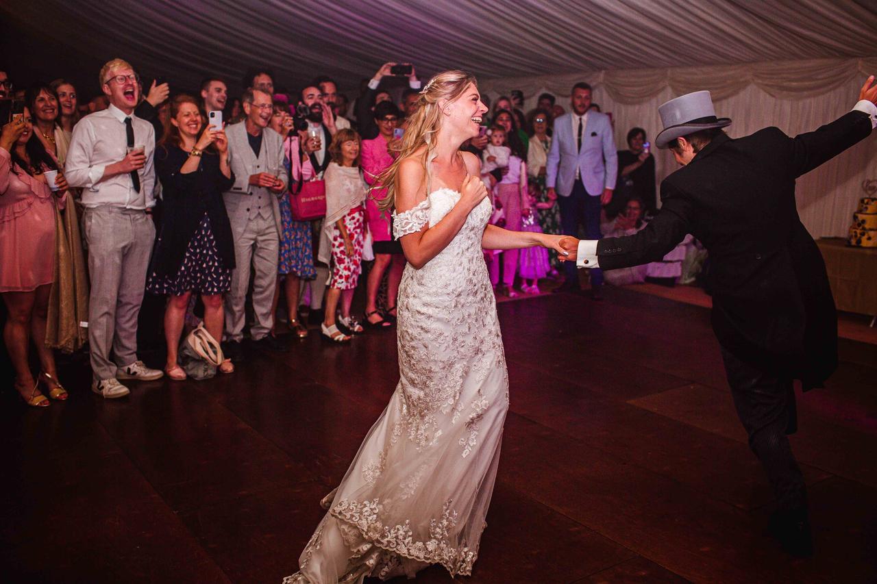The bride and groom laugh and dance as their guests watch on