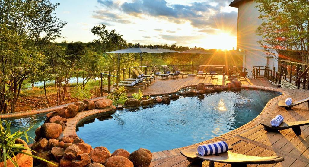 Victoria Falls Safari Club, a luxurious hotel displaying sunloungers, a swimming pool and a view of the African Bush