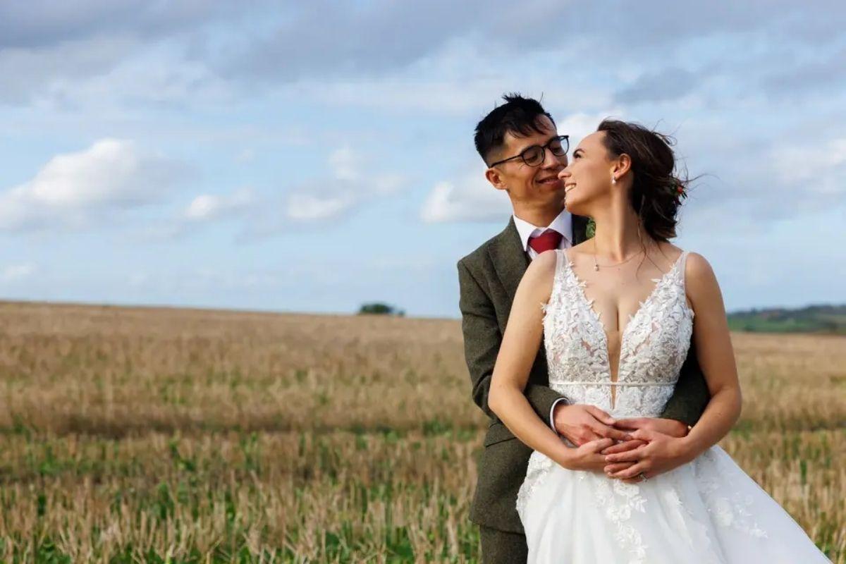  a bride and groom with their arms around the bride's waist posing in a field of grass