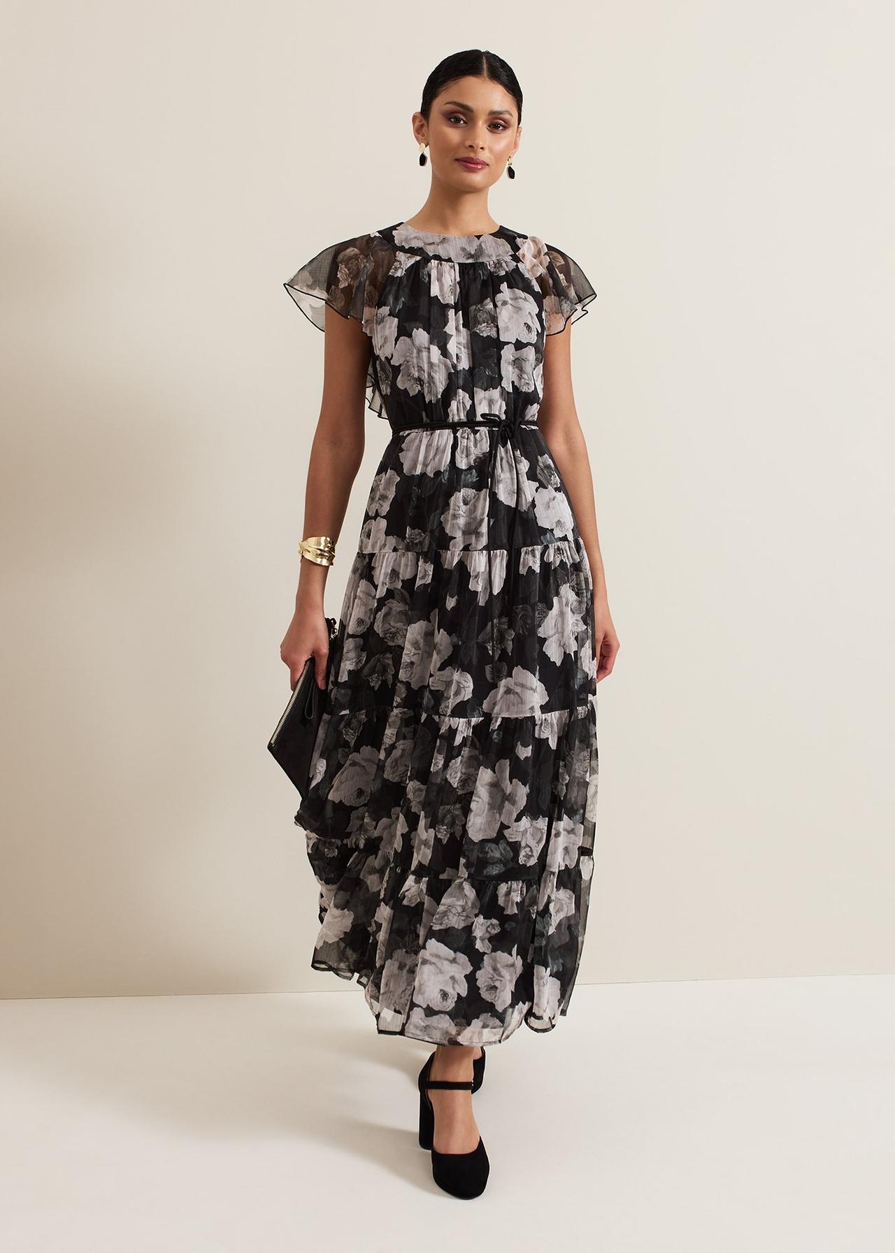 a wedding guest wearing a black and ivory floral print maxi with short sheer sleeves with frill detail and a tiered skirt. She is wearing it with black shoes and accessories.