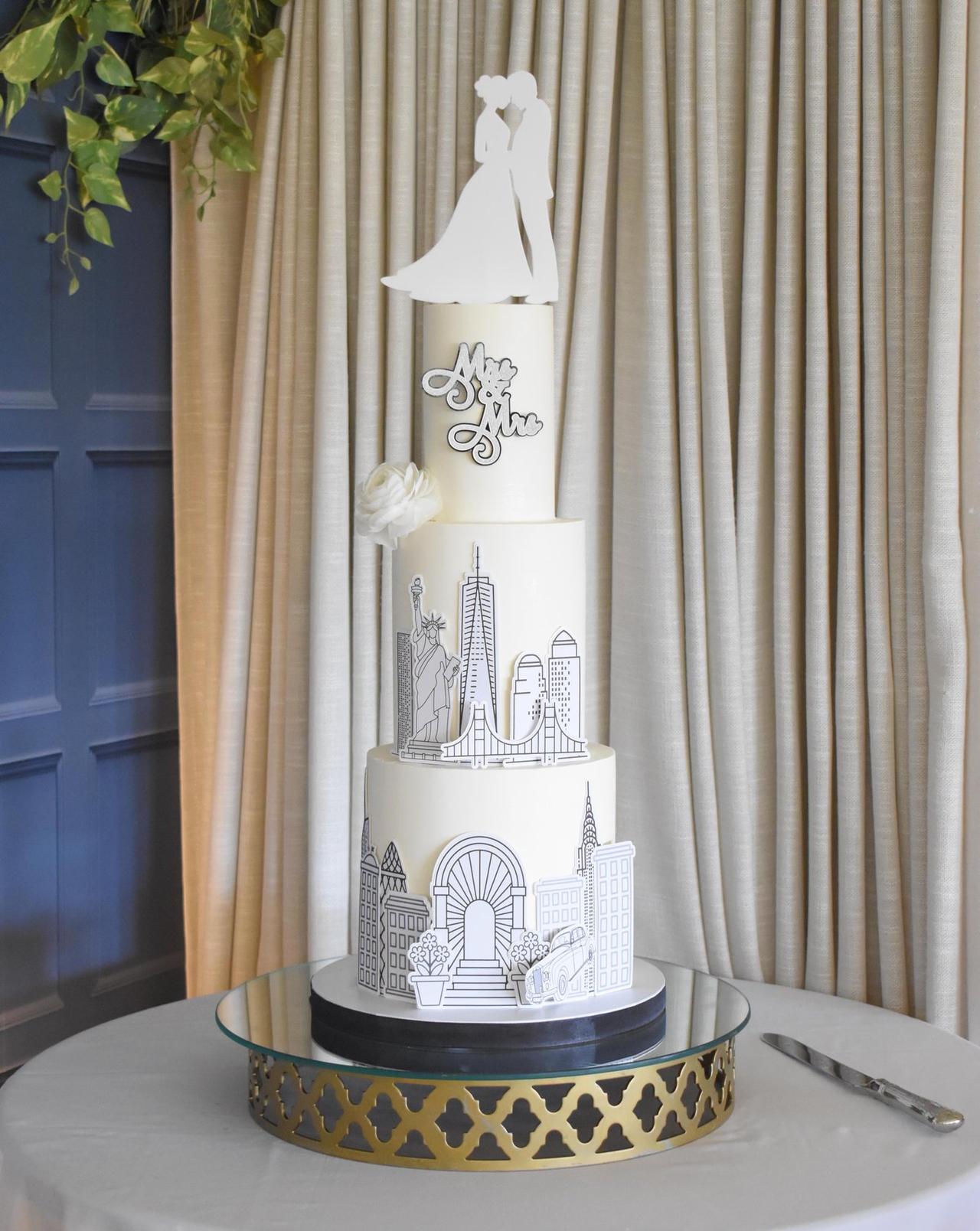 A three tier white iced wedding cake with sugar paper stencilled cityscape detail.
