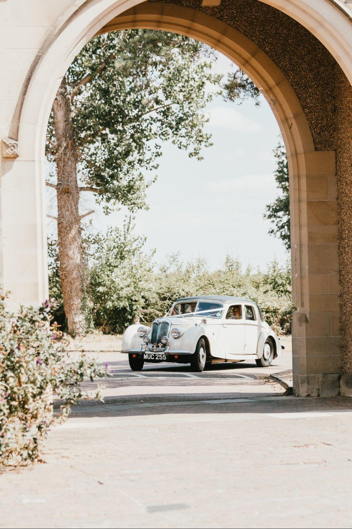 A white wedding car drives under an archway