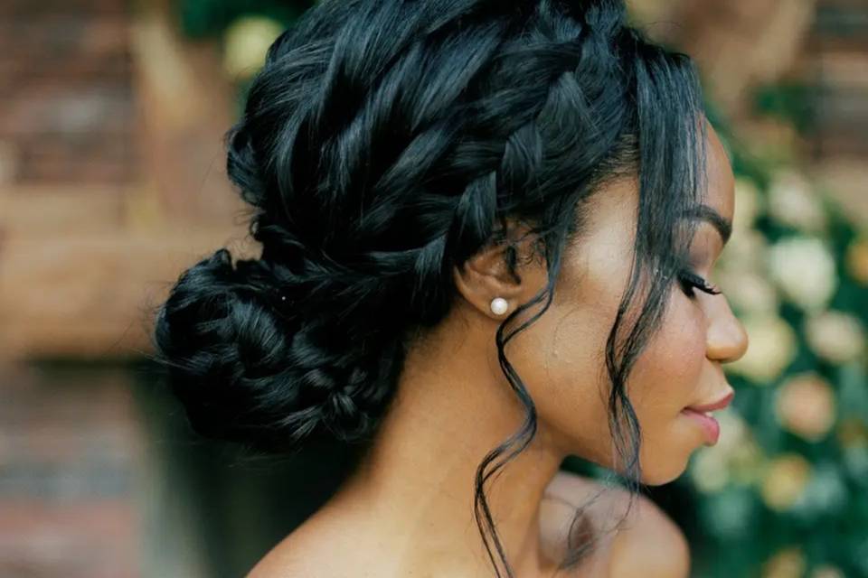 side view of a low bun with braids leading into it and a single curl hanging at the front
