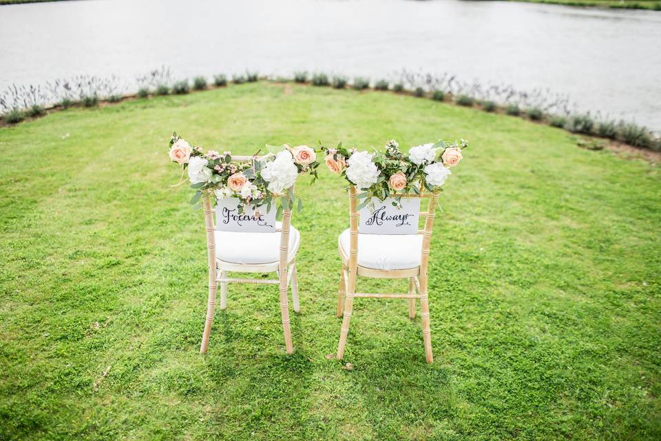 Two flower-covered wedding chairs on a remote, grass-covered cliff, one which reads 'Forever' and the other 'Always'