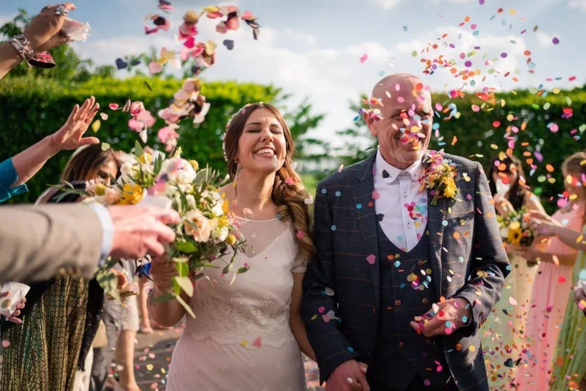 guests throw colourful confetti over a bride and groom after they got married in a country venue