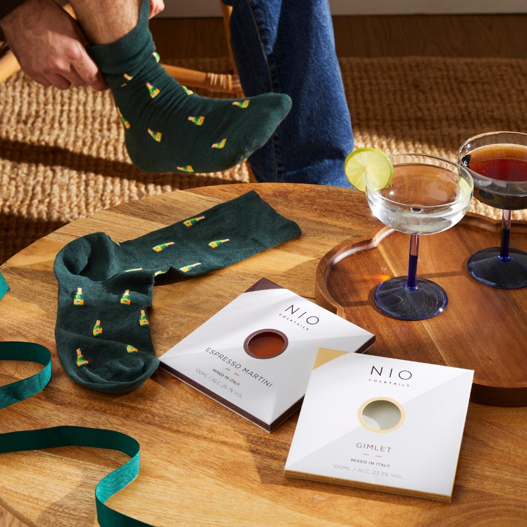 A best man pulling on a pair of champagne bottle-print socks; there are cocktails on the table next to him.