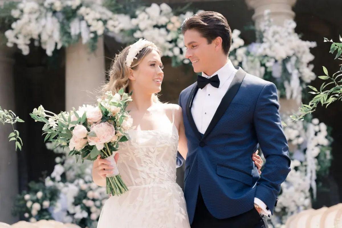 a bride and groom smiling at each other whilst holding the bride's bouquet and matching flowers are in the background