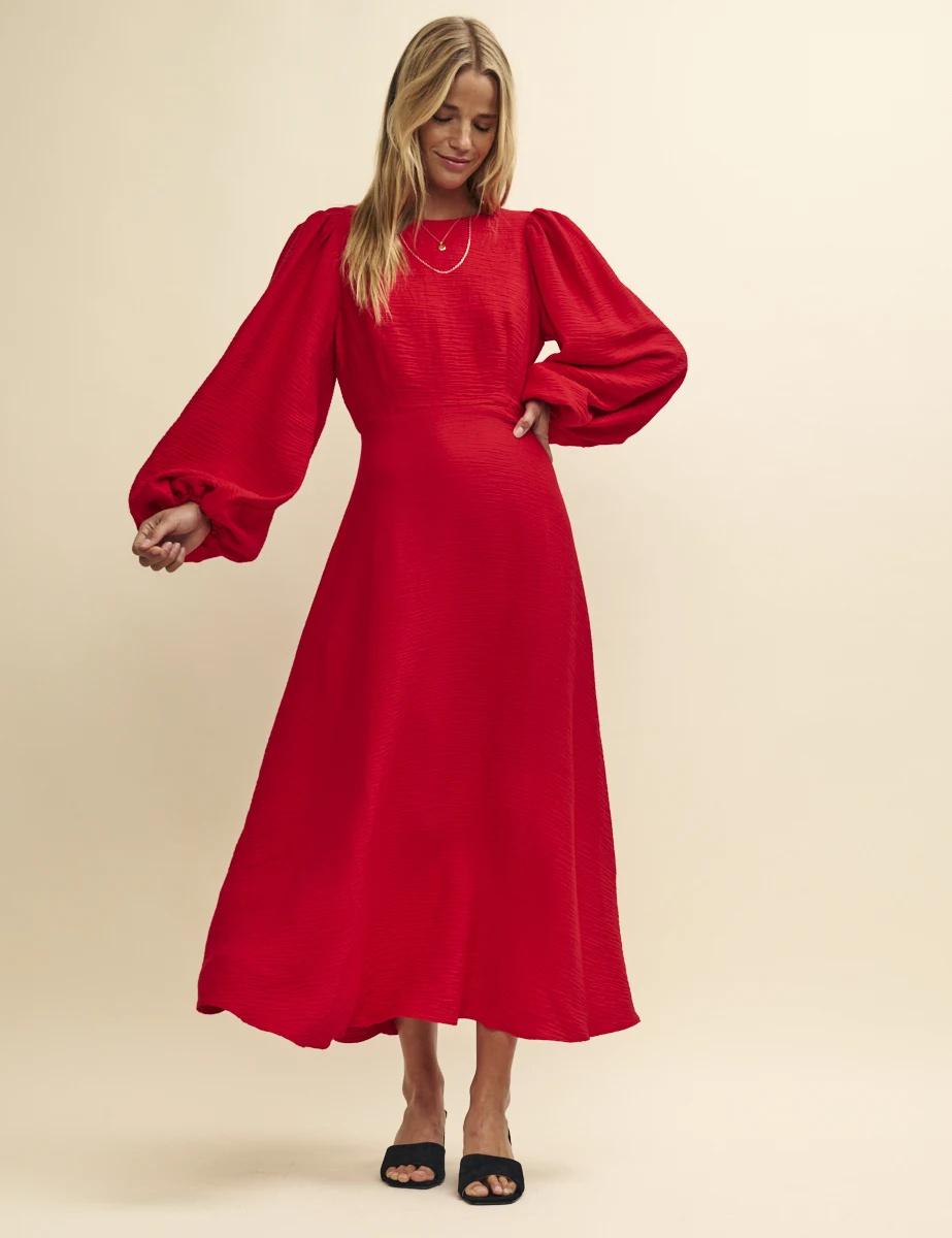 A wedding guest wearing a red midi dress with long balloon sleeves.