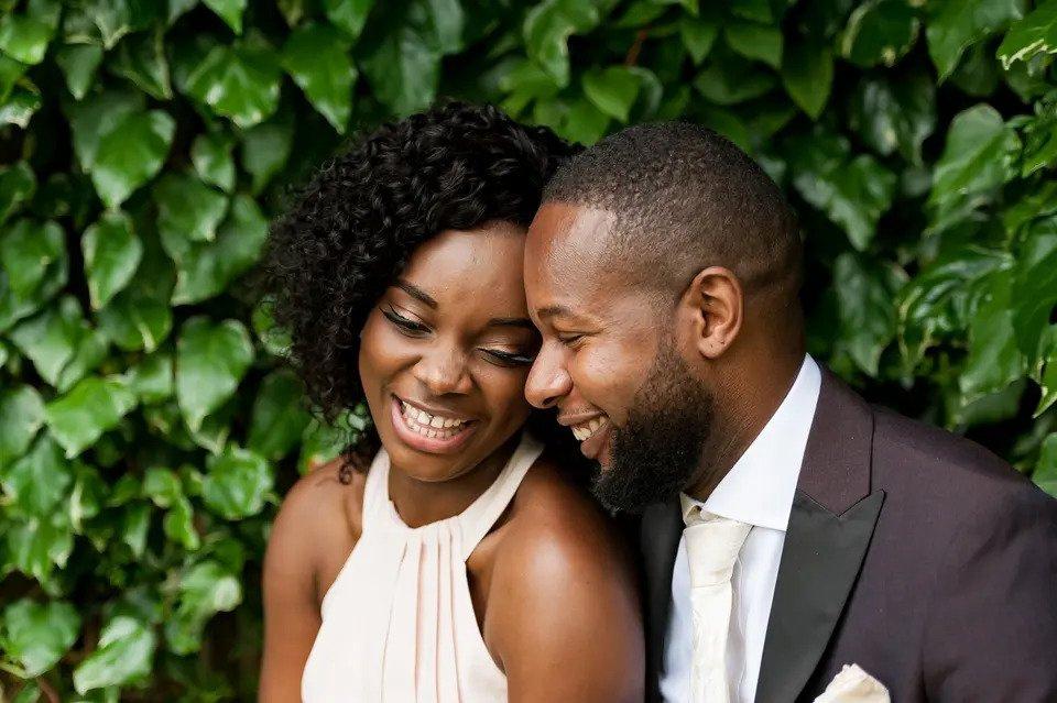 bride and groom embrace and laugh candidly outdoors against a background of green leaves