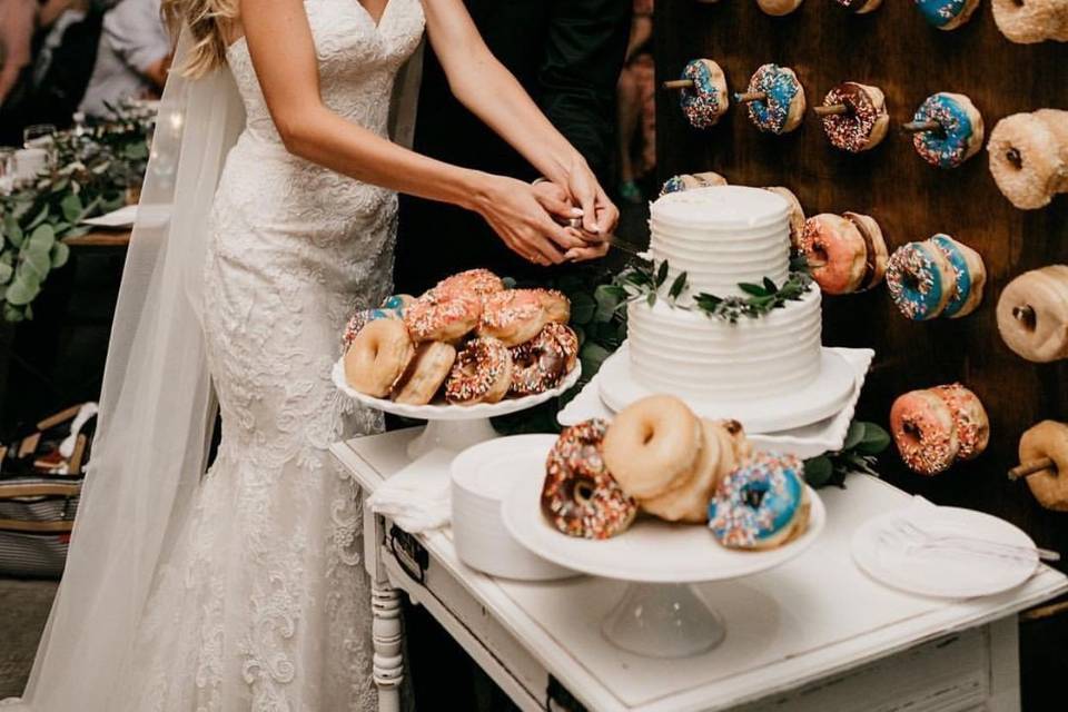 Couple cutting a cake next to a donut wall