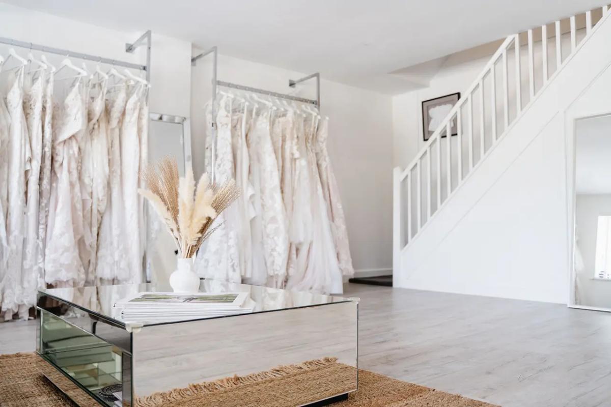 The inside of a weding dress boutique with a white staircase and a rack of beautiful white wedding dresses