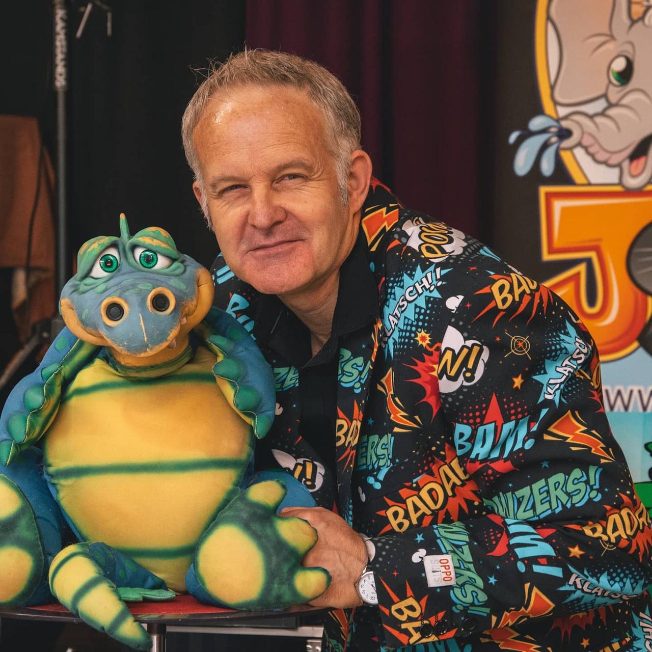 A children's wedding entertainer wearing a colourful jacket and posing with an alligator puppet