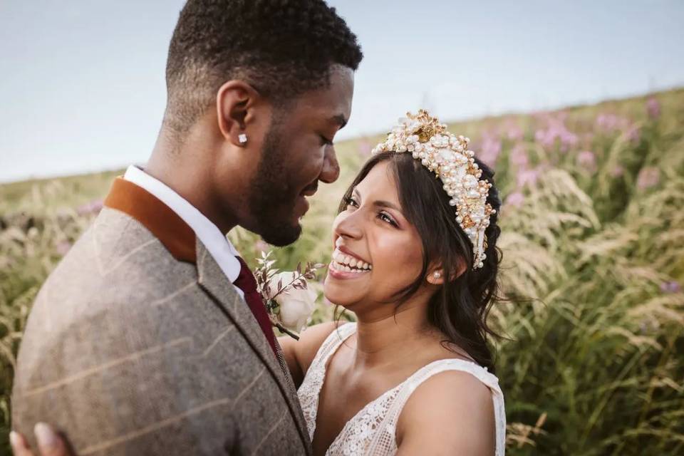 A bride and groom at their summer wedding looking at each other smiling with fields in the background