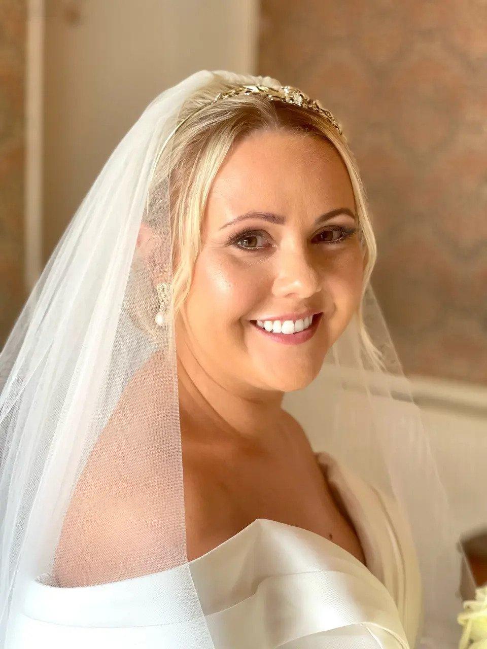 A smiling bride looks over at the camera with a veil and picture-perfect makeup