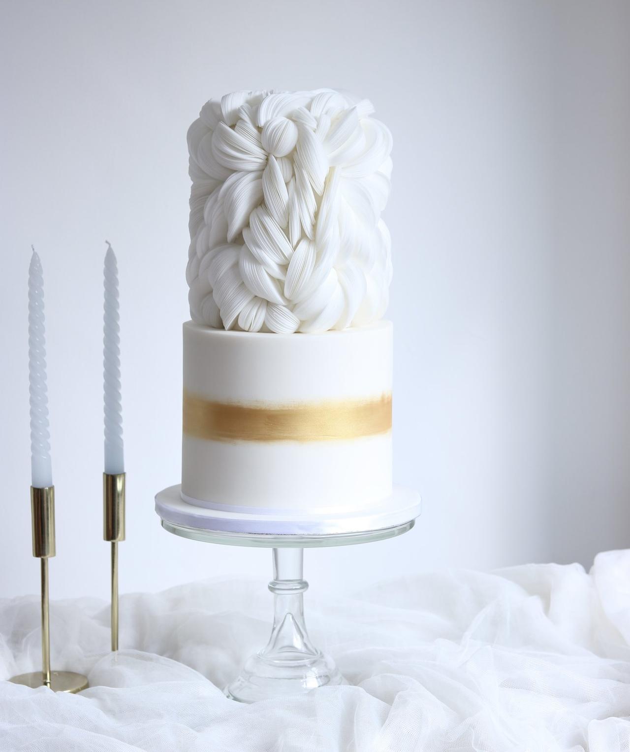 A simple white and gold wedding cake with ruffled, feather-like top tier detail.