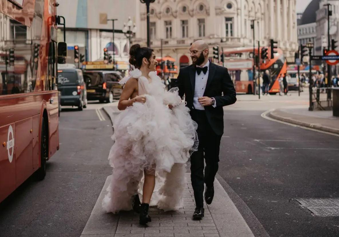 https://cdn0.hitched.co.uk/article/3540/original/1280/jpg/130453-bride-in-ruffled-wedding-dress-walking-through-central-london-with-her-groom.jpeg