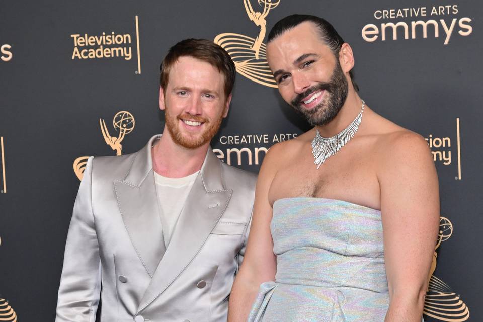 Jonathan Van Ness wears a strapless silver maxi dress and matching necklace next to his husband Mark Peacock wearing a satin champagne-coloured suit at the Emmys