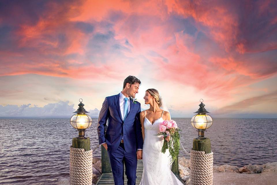 Newlyweds on a dock on the beach at sunset