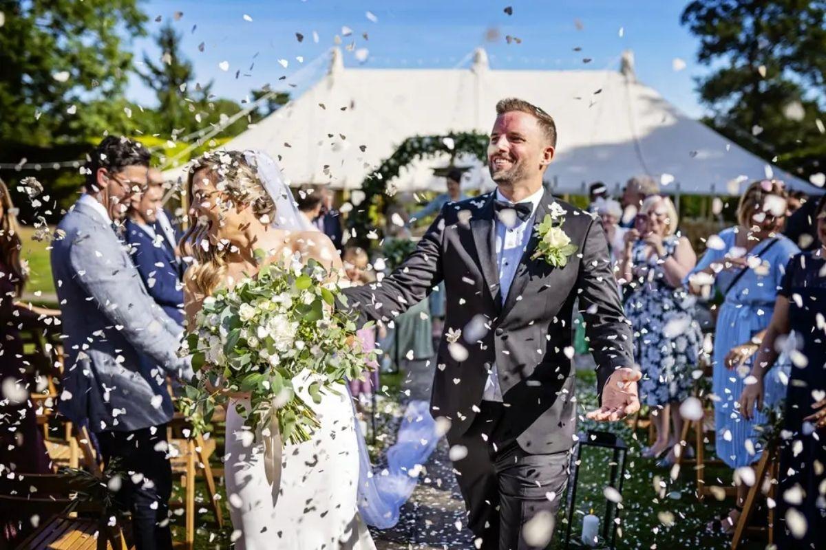 a couple laughing and celebrating as their wedding guests shower them with colourful confetti