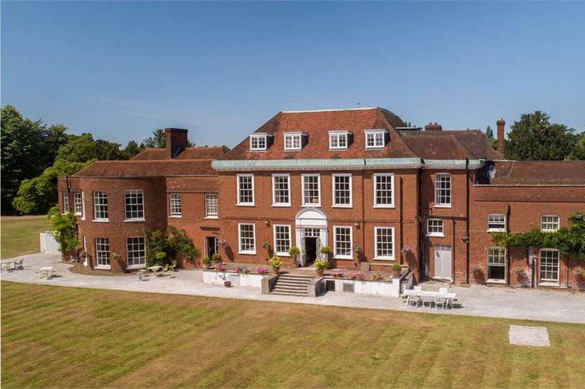 Three storey red brick country house wedding venue with patio furniture, a manicured lawns and plants
