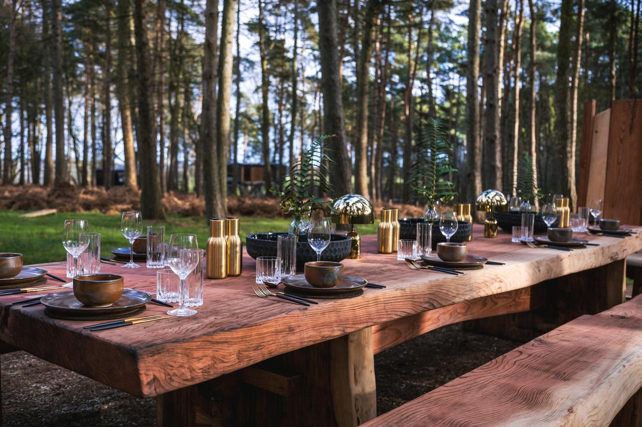 A large oak table decorated for a wedding in the middle of the forest with benches either side
