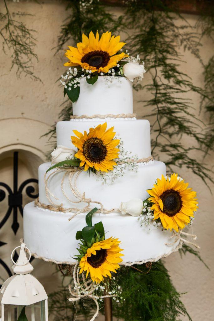 Four tiered white rustic wedding cake with sunflowers and twine