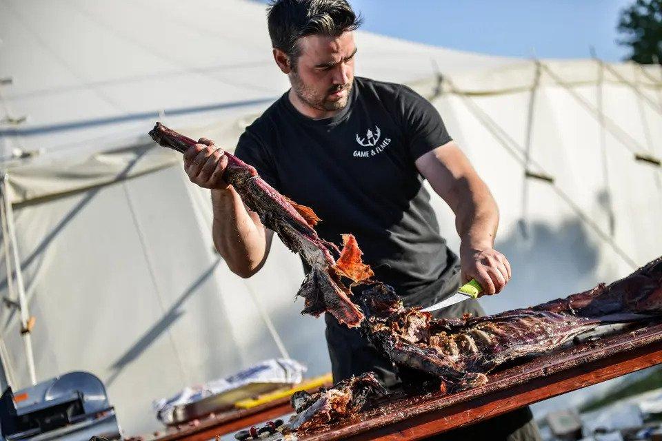A man standing in front of a tipi carving up a hog roast
