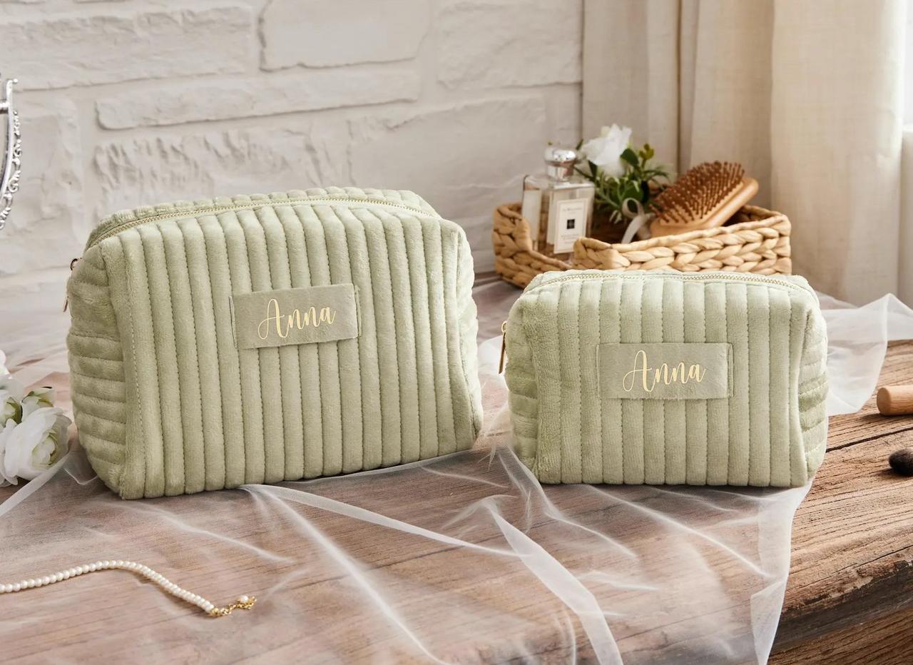 Two sage green velvet make-up bags on a dresser, personalised with the name 'Anna'.