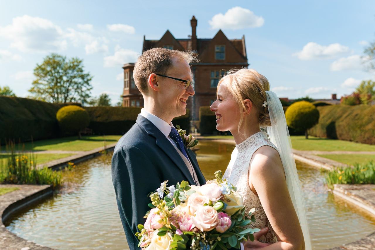 bride and groom outside in front of a stately home, smiling in the sun