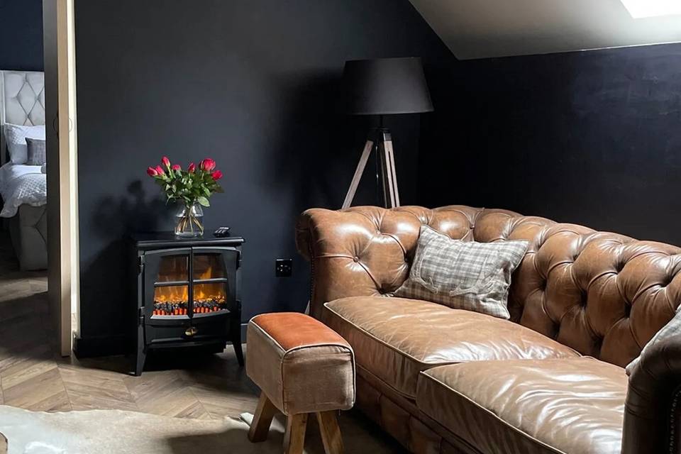 A cosy cottage living room with a brown leather sofa and footstool in front of a woodburning stove with a fire burning