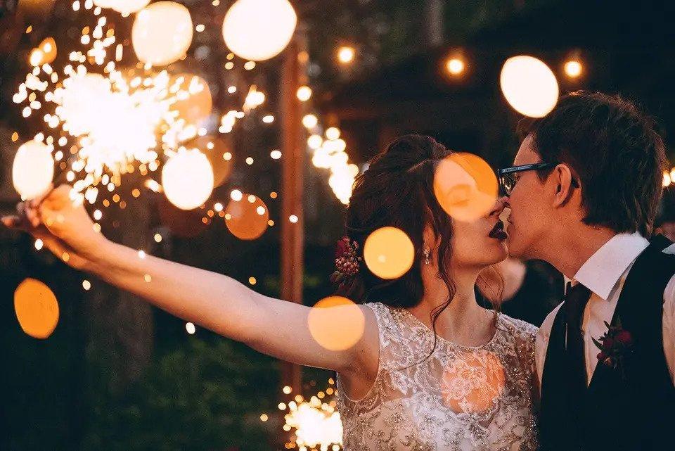 Bride and groom embrace while the bride holds a sparkler behind her