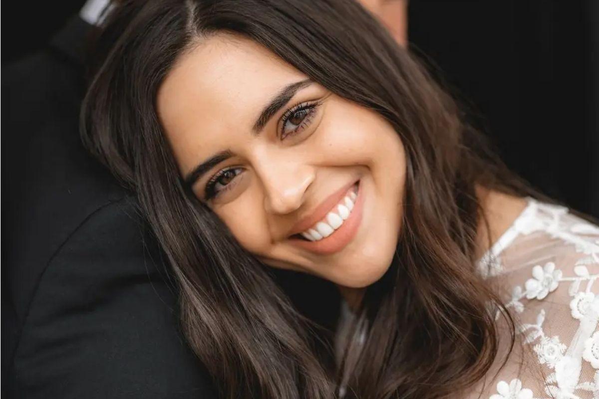 a bride resting her head on her groom's shoulder smiling and showcasig her lace wedding dress