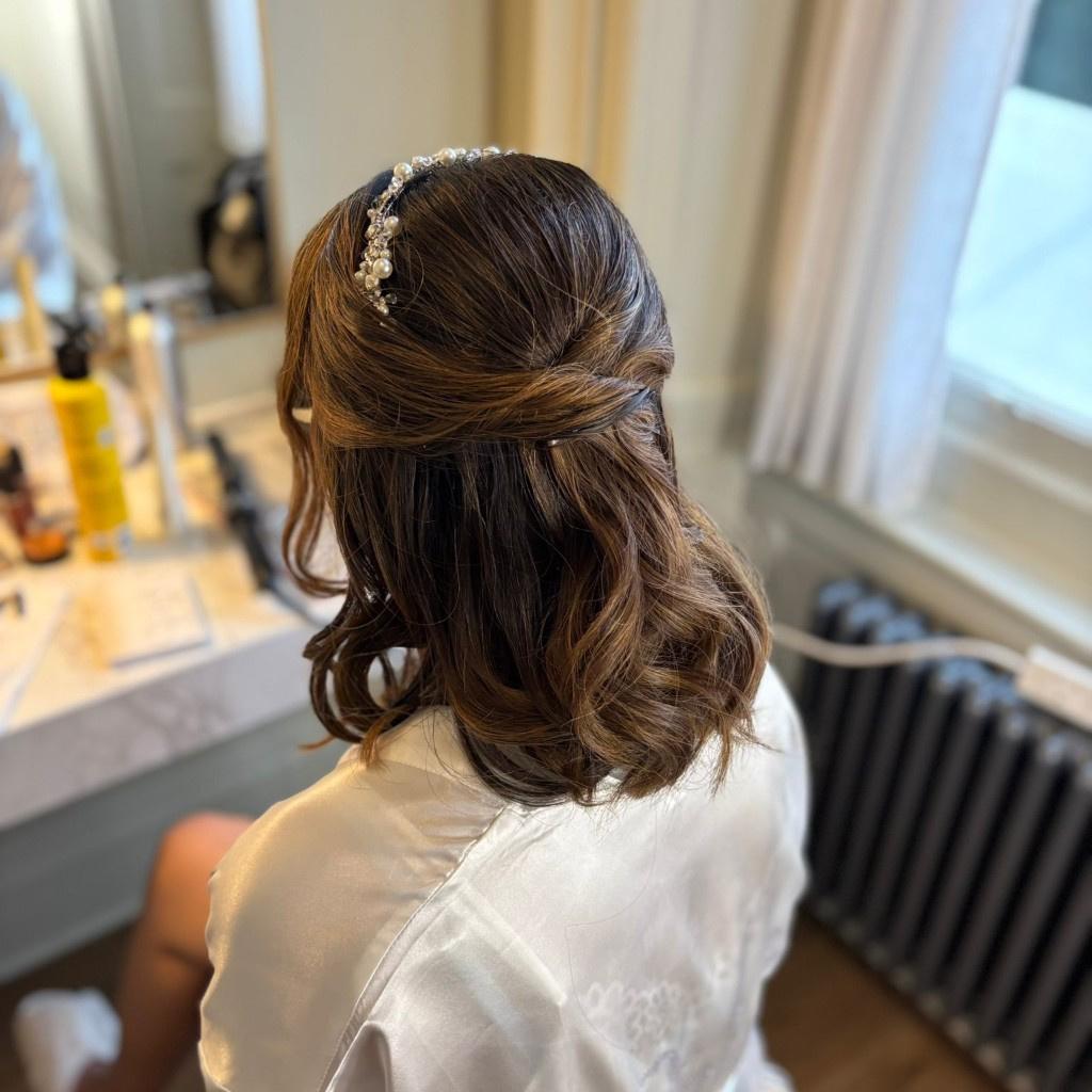 A bride with short brown hair getting her hair done into a half up do with a pearl tiara 