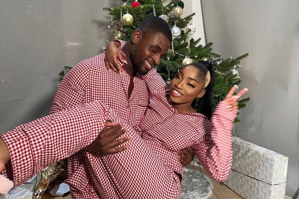Dami holding Indiyah in matching pyjamas in front of a Christmas tree, both smiling 