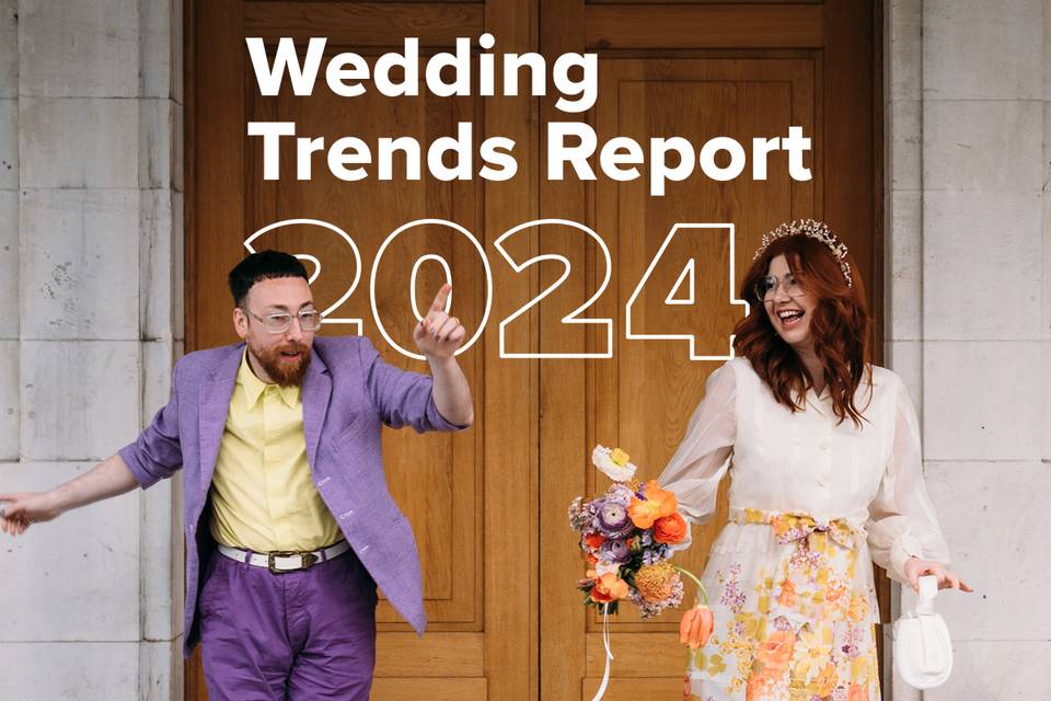 Couple in colourful wedding clothing - the groom wears a lilac suit and yellow shirt, and the bride wears a white blouse with an orange floral skirt - posing and dancing together joyfully outside of a town hall venue with '2024 wedding trends' super imposed behind them in white text