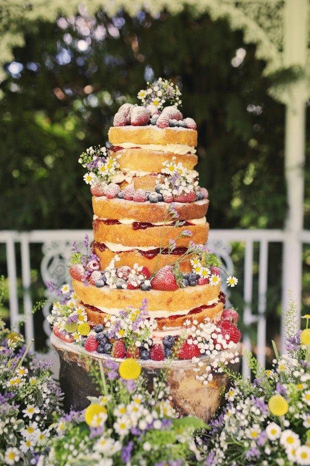 Three tiered victoria sponge rustic wedding cake with icing sugar, daisies and fruit