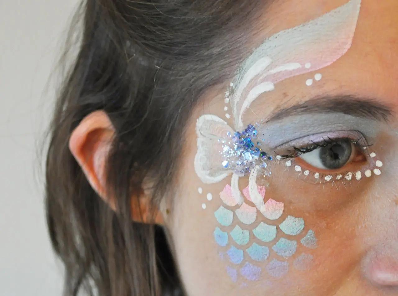 Close up image of a beautiful blue butterfly face paint design around a woman's eye, studded with jewels and glitter