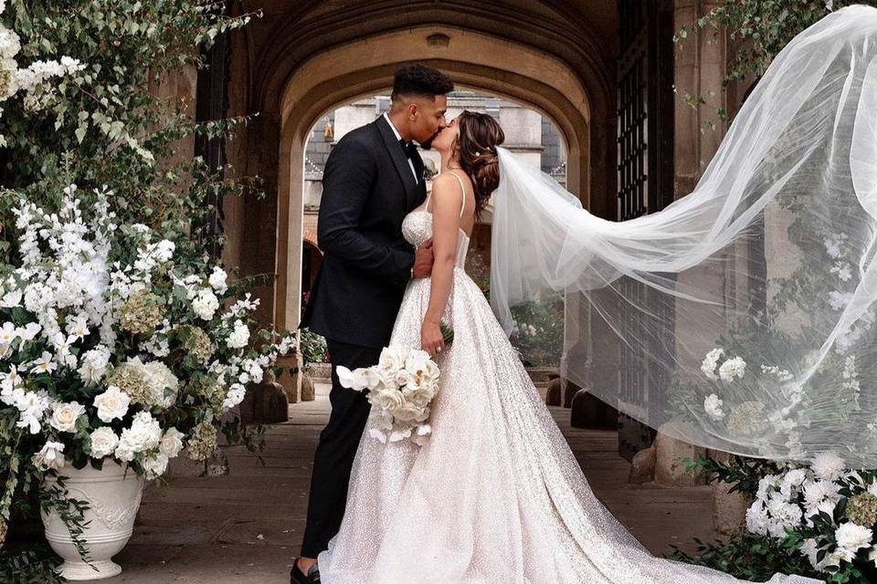 Naomi and Jordan Banjo kissing on their wedding day with Naomi's veil in the air, showcasing her sparkly Berta wedding dress