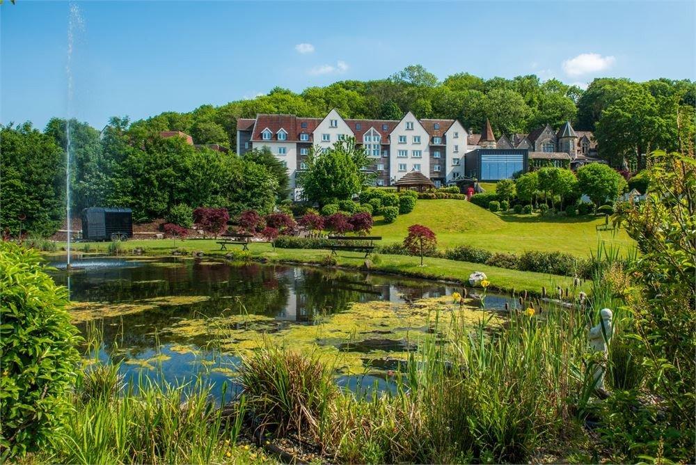 Grand 5 storey country house photographed from across a pond with fountains and manicured gardens